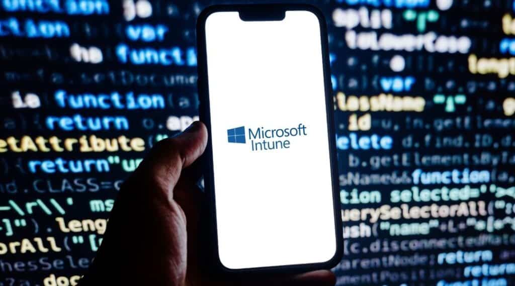 Main tenant un smartphone affichant le logo Microsoft Intune, devant un écran de code informatique en arrière-plan, illustrant la gestion et la sécurité des appareils professionnels